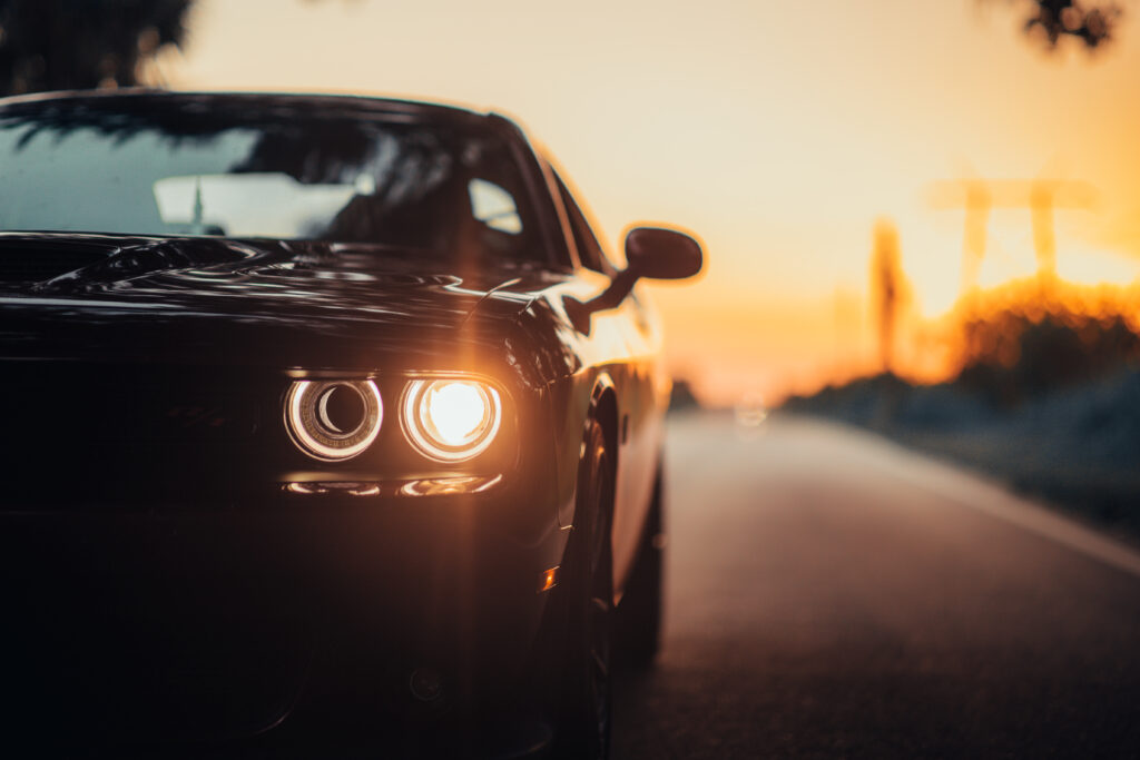 A luxurious car parked on the highway with an illuminated headlight at sunset
